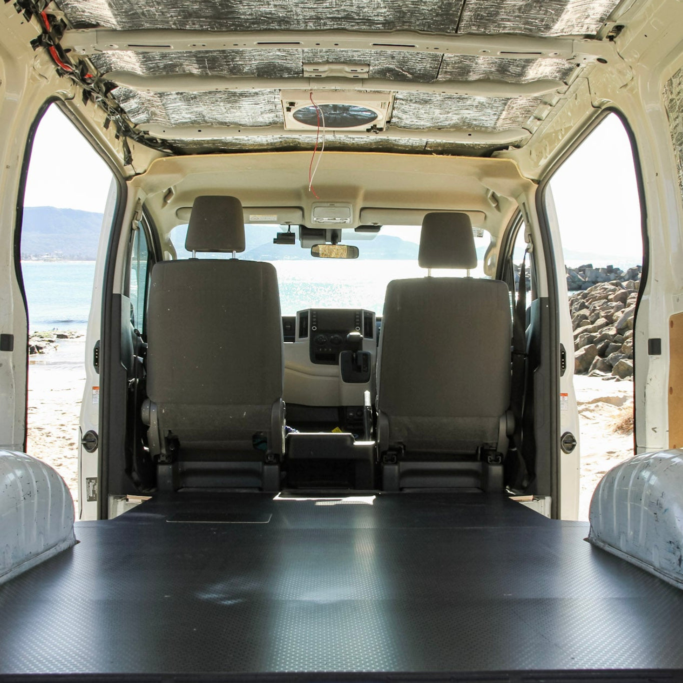 Van interior with a flatbed and white seats, showing a desert landscape outside.