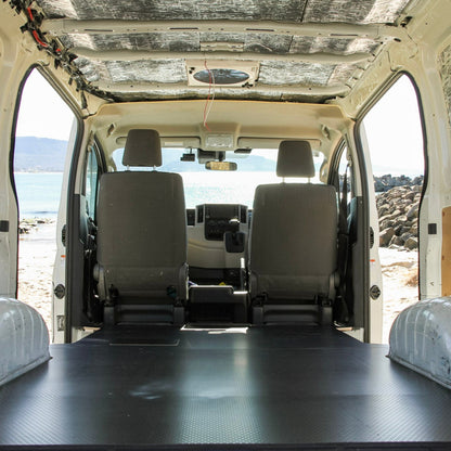 Van interior with a flatbed and white seats, showing a desert landscape outside.